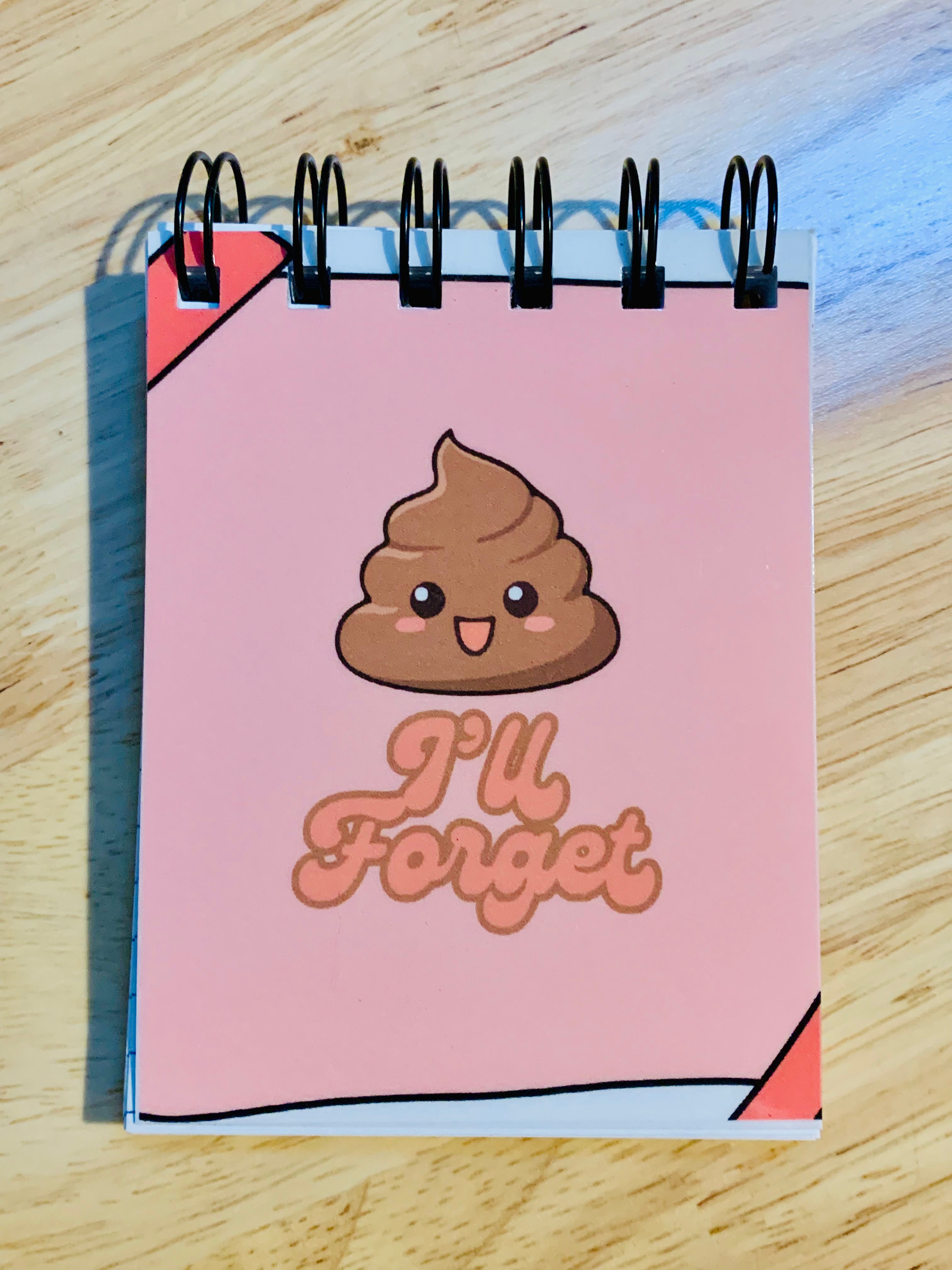 Notebook with a cartoon poop emoji and 'I'll Forget' text on a wooden surface
