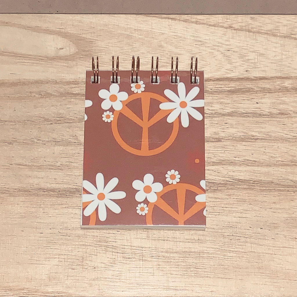 Small spiral-bound notebook with peace symbol and flower design on a wooden surface