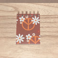 Small spiral-bound notebook with peace symbol and flower design on a wooden surface