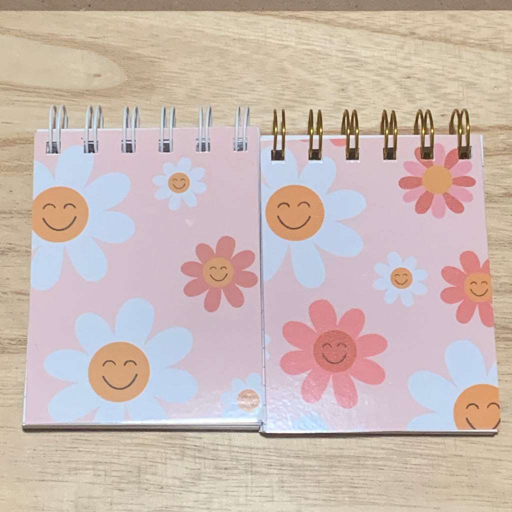 Two spiral-bound notebooks with floral designs on a wooden surface