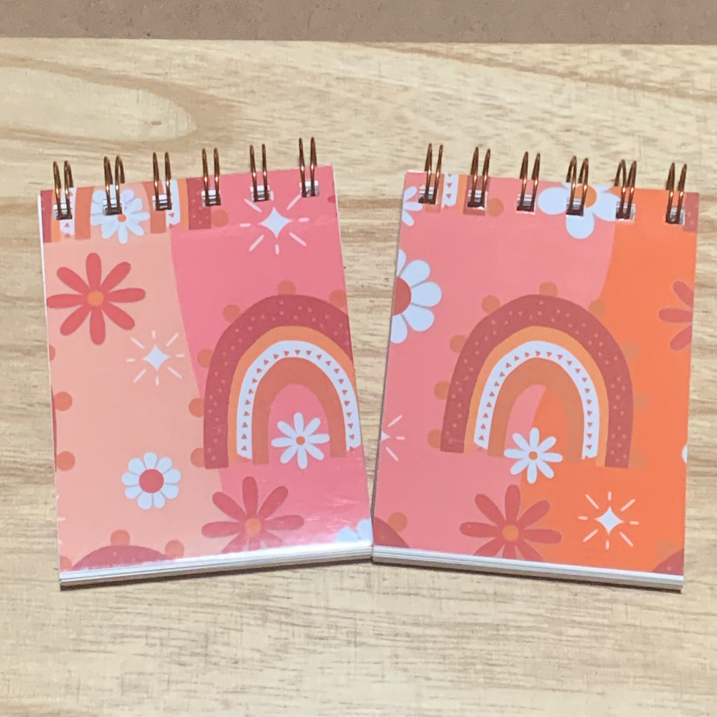 Two small spiral-bound notebooks with colorful boho designs on a wooden surface