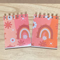 Two small spiral-bound notebooks with colorful boho designs on a wooden surface