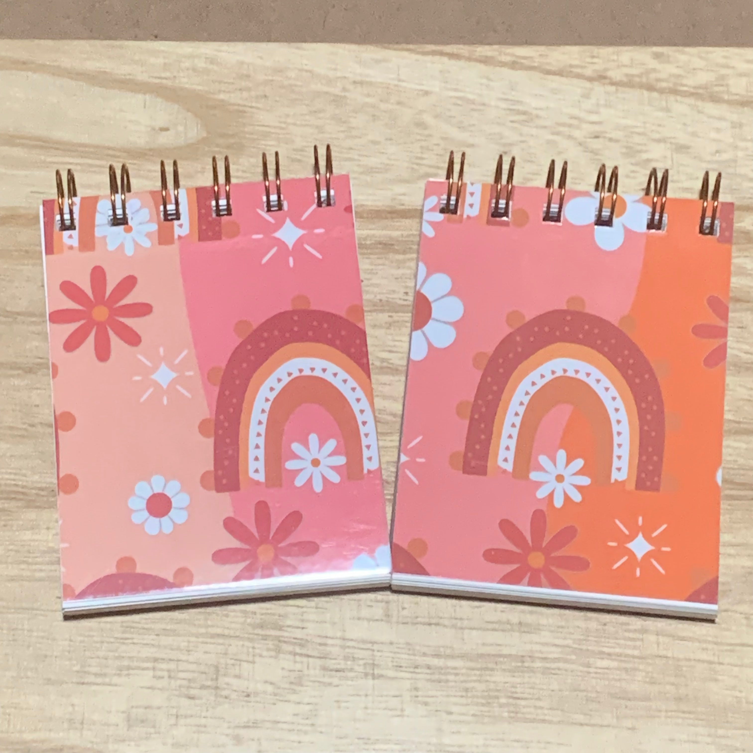 Two small spiral-bound notebooks with colorful boho designs on a wooden surface