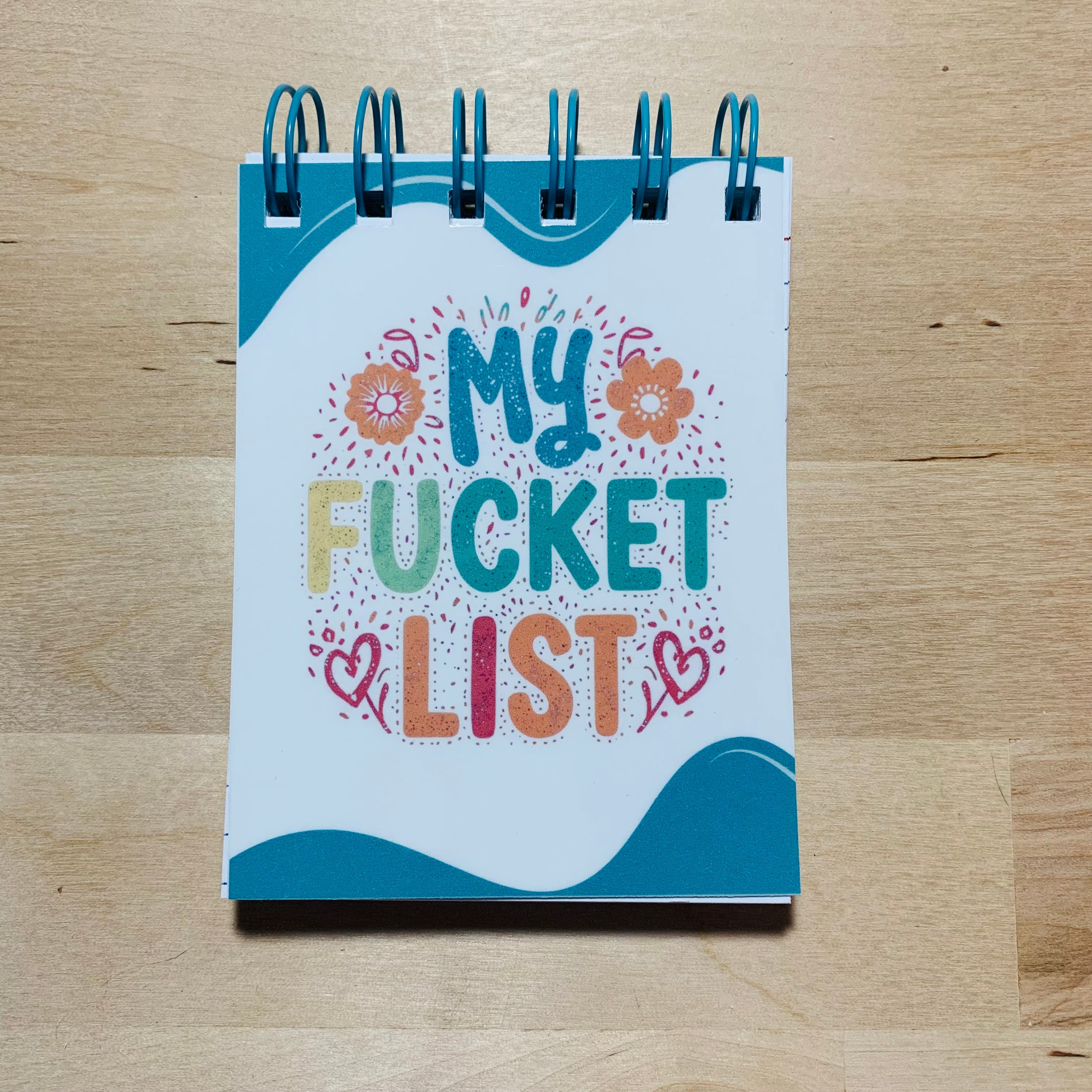 Notebook titled 'My Fucket List' on a wooden surface