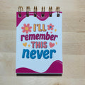 Small notebook with 'I'll remember this never' text on a wooden surface