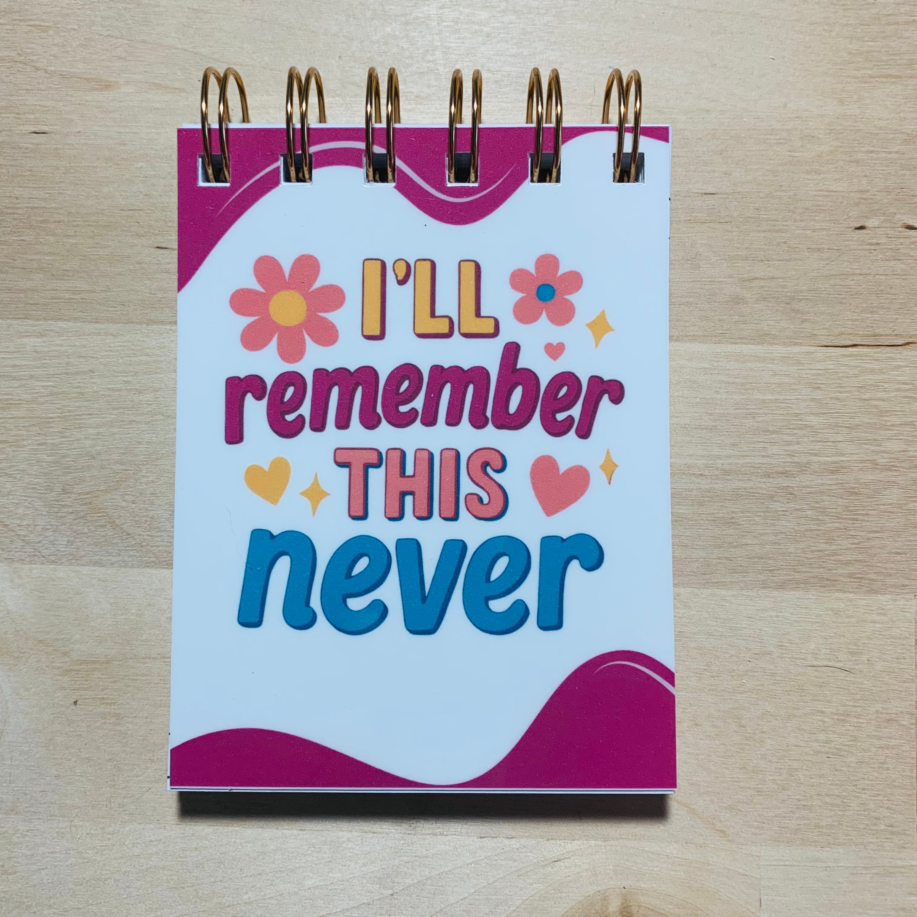 Small notebook with 'I'll remember this never' text on a wooden surface