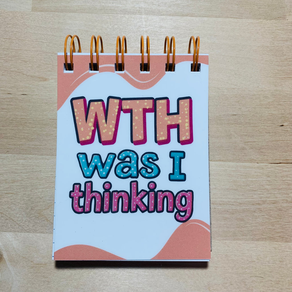 Notebook with 'WTH was I thinking' text on a wooden surface