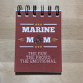Notebook with 'Marine Mom' text and logo on a wooden surface