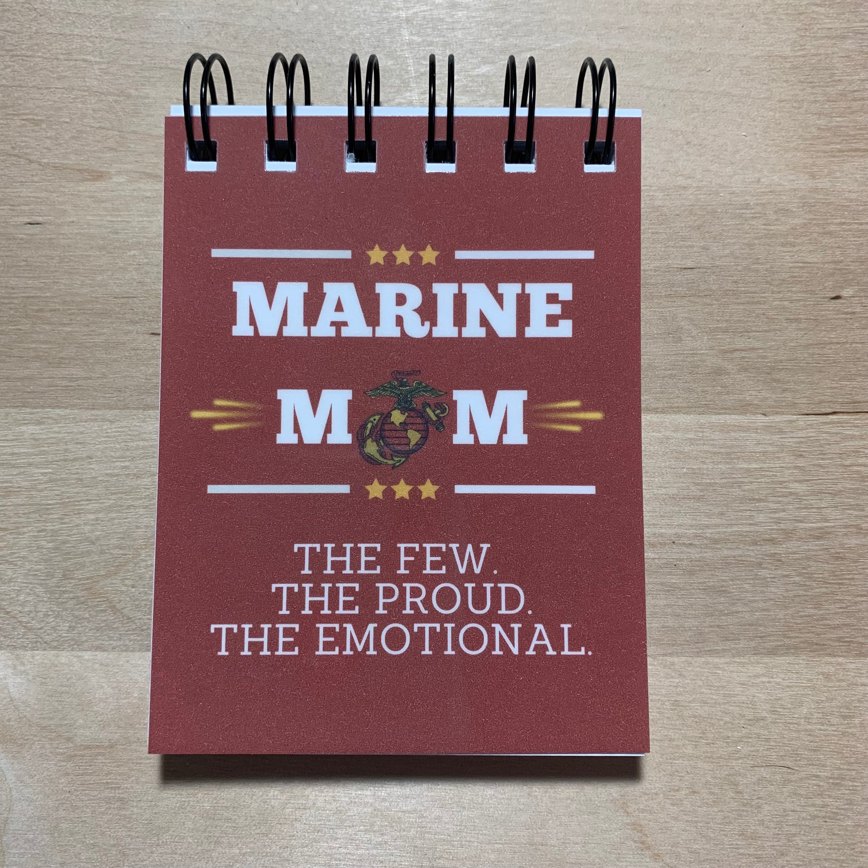 Notebook with 'Marine Mom' text and logo on a wooden surface