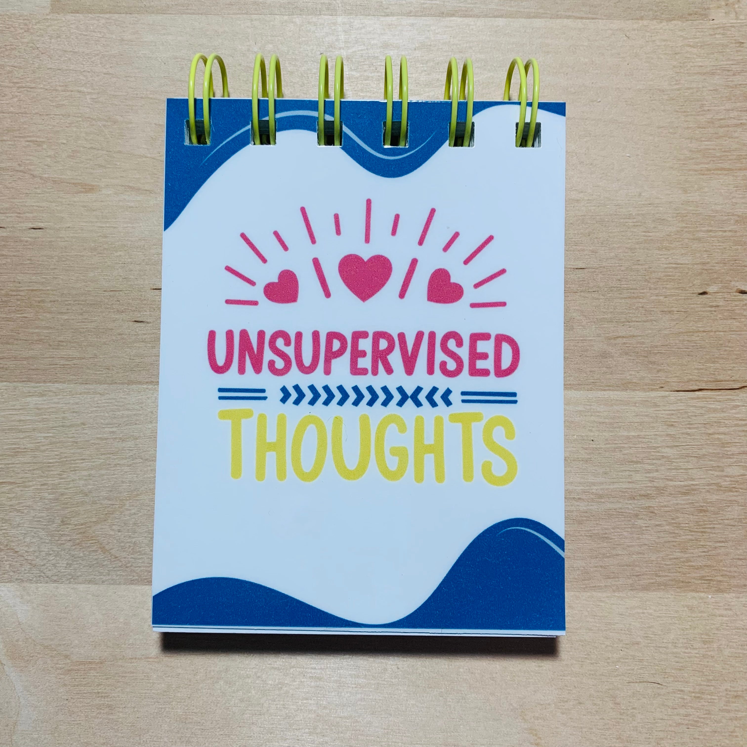 Notebook with 'Unsupervised Thoughts' on a wooden surface