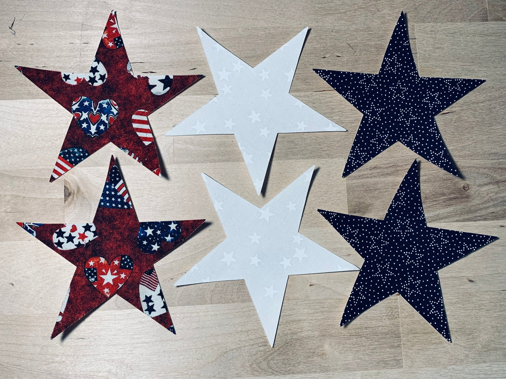 Five star-shaped decorative items on a wooden surface, with patterns resembling American flags.
