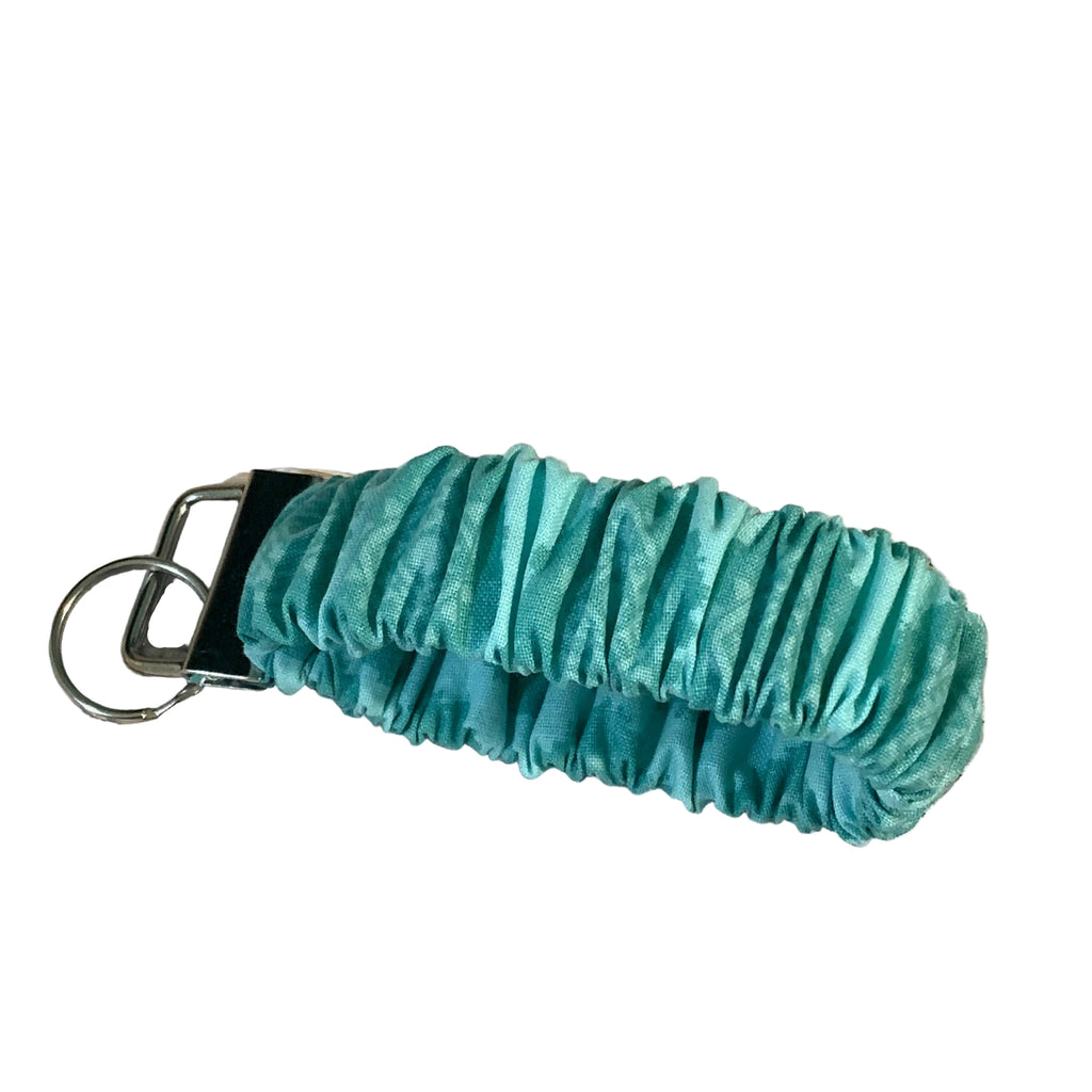 Teal scrunchie with keychain on a woven surface with flowers in the background