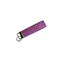 Purple key fob with gold pattern on a light wooden surface with pink flowers.