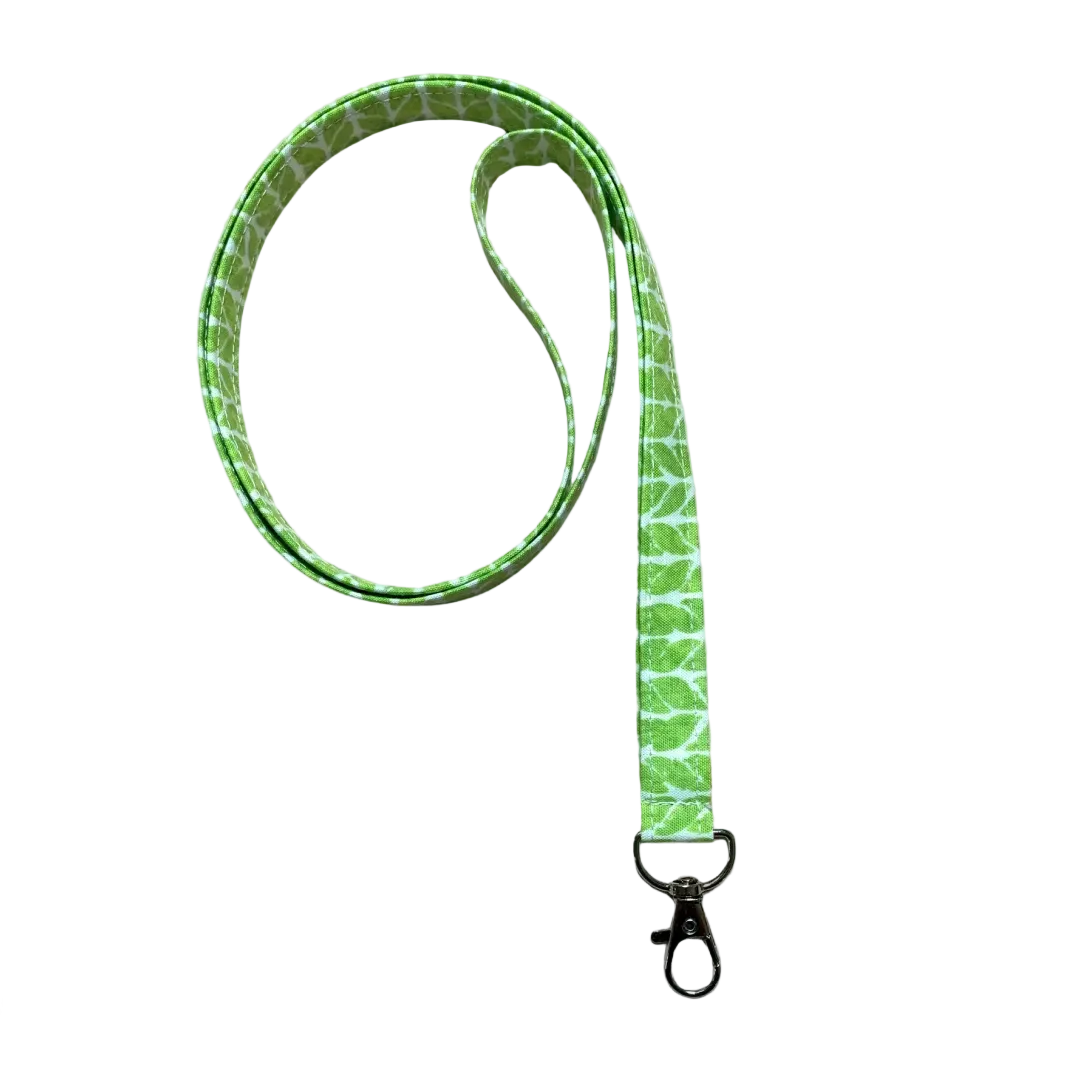 Green patterned lanyard with a clip on a light wooden surface with pink flowers.