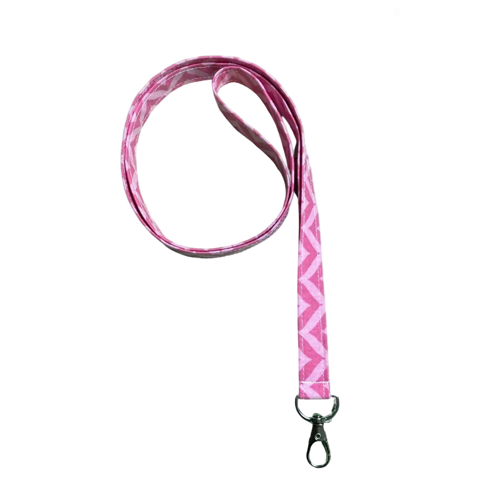 Pink lanyard with geometric pattern on a light wooden surface with pink flowers.